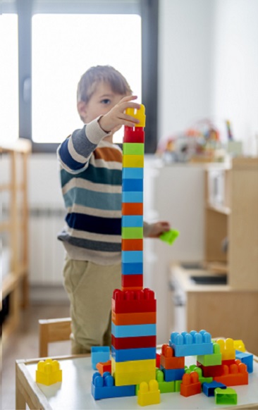 A child in a striped blue shirt stacks blocks as tall as their head