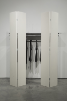 Photo of art installation: closet with white doors and black shirts hanging inside