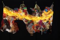 Mixed media textile hanging collage made up of a patchwork of multi-colored fabrics, textural attachments and lights.