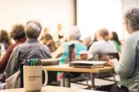 Adults sitting at desks in a classroom type setting. They face away from the camera.