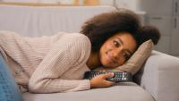 A person laying on their side on a couch holding a remote and smiling