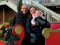 a woman, man and baby pose for a photo in a red holiday sleigh