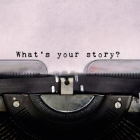 A typewriter with paper in it. The paper reads "What's your story?"