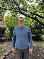 Jared Campbell man standing outside in a light blue sweater, glasses, grey pants