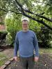 man standing outside in a light blue sweater, glasses, grey pants